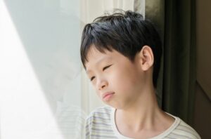 Anak kecil kecewa bersandar di dinding dengan ekspresi sedih, menggambarkan perasaan frustrasi atau kekecewaan.