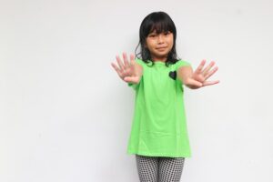 Anak kecil tersenyum sambil melambaikan tangan, menunjukkan keceriaan dan keramahan. Ideal untuk tema pendidikan, perkembangan anak, atau kebahagiaan keluarga.