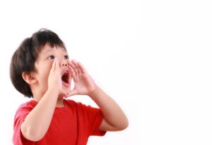 Anak kecil sedang berteriak sambil menggunakan tangannya untuk mengekspresikan emosi, menggambarkan antusiasme atau komunikasi aktif.