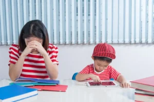 Gambar seorang anak kecil sedang bermain tablet dan seorang ibu sedang memikirkan sesuatu